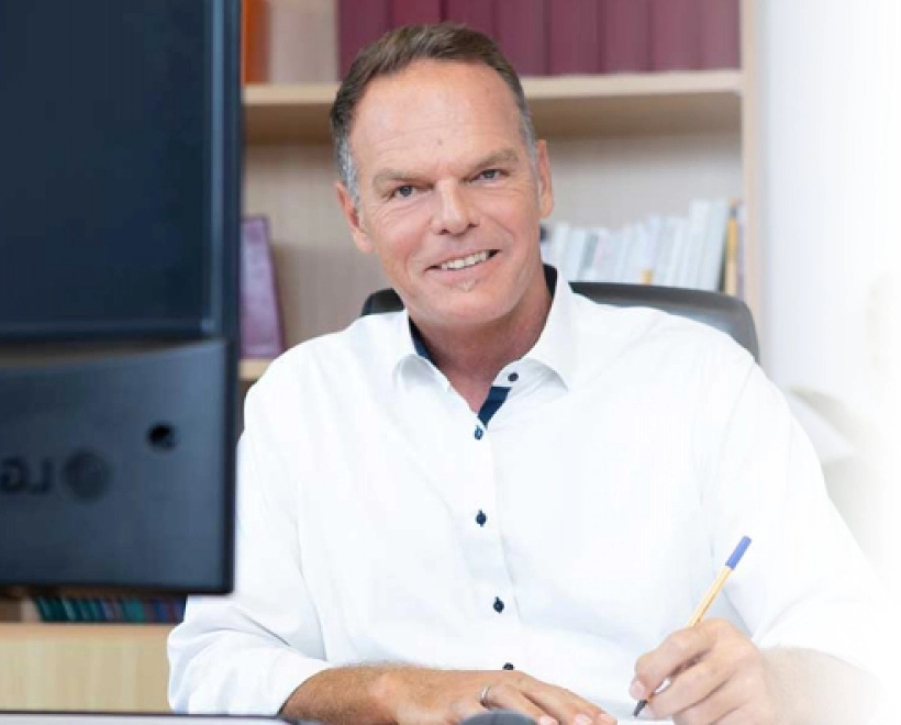 Lächelnder Steuerberater Stefan Hinterleitner im weißen Hemd am Büro-Arbeitsplatz zur Immobilienberatung.